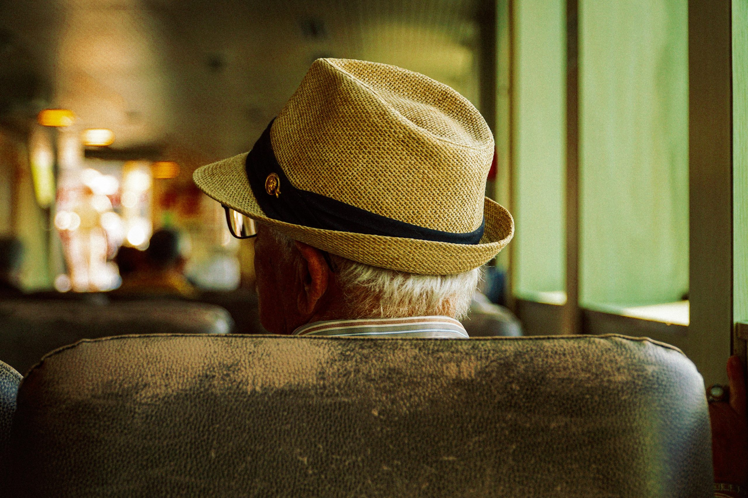 Begleitung im Urlaub Back view of a senior man in a hat seated on a train, emphasizing travel and leisure.