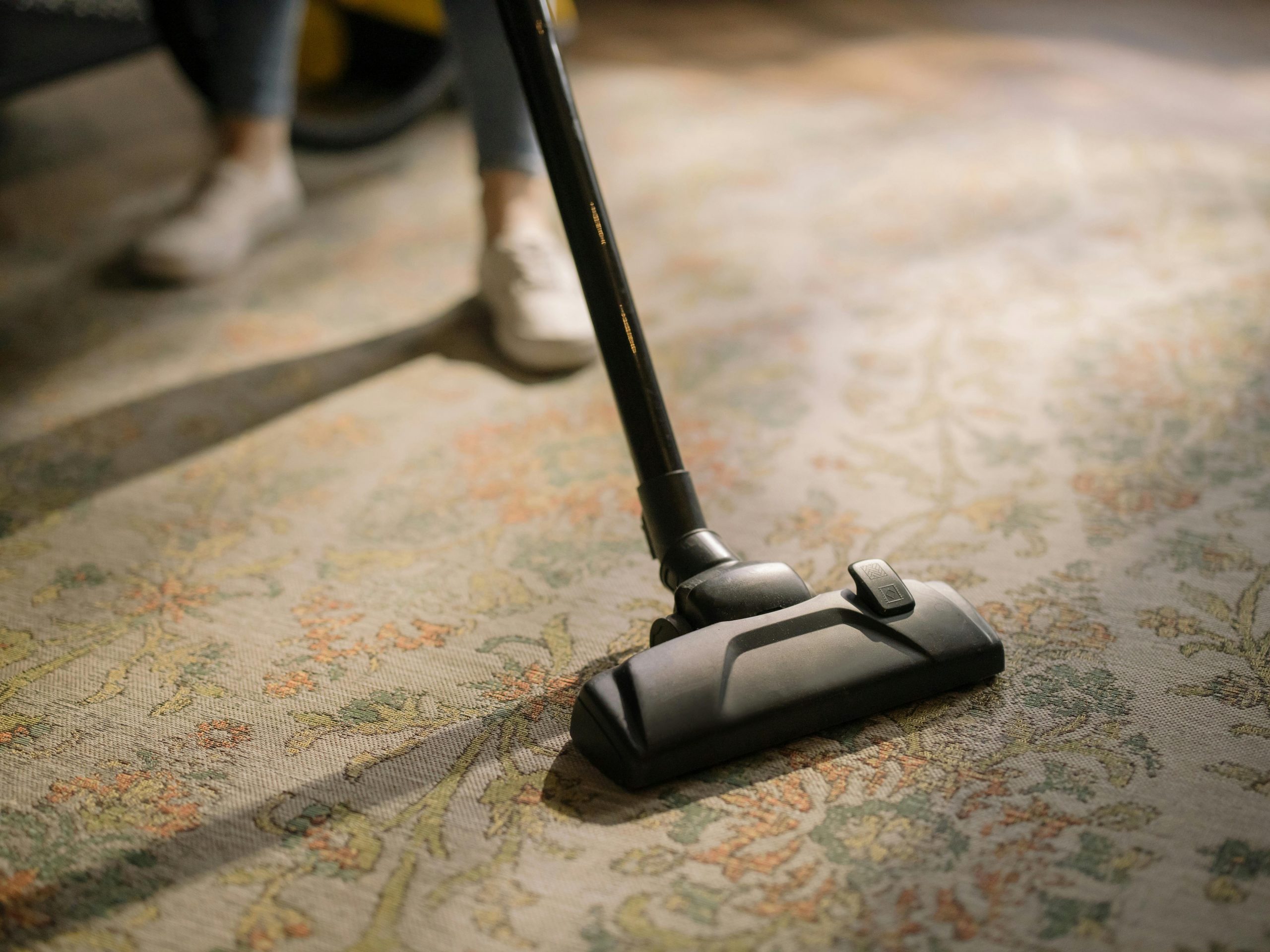 Haushaltshilfe Close-up of a vacuum cleaner on a patterned carpet in a sunlit room, capturing a moment of household cleaning.
