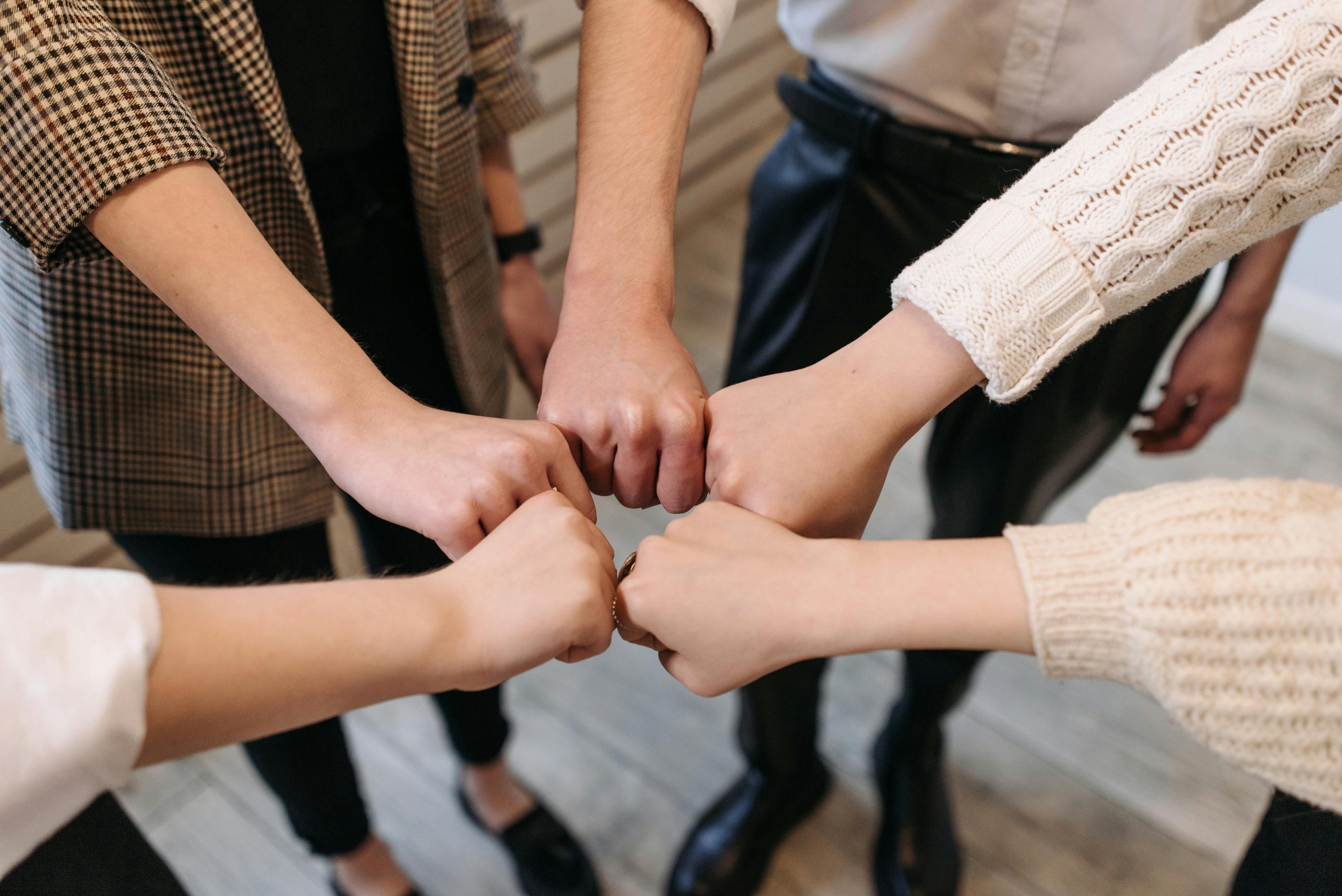 Hol di toi gUG | Soziale Hilfe, Integration & Gemeinschaft Five people uniting hands indoors, symbolizing teamwork and unity.