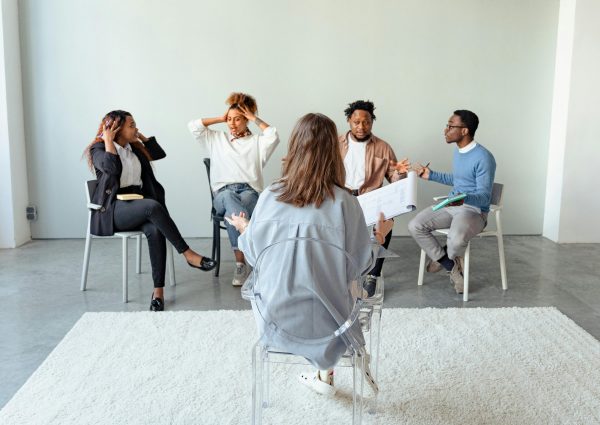 People engaging in a group therapy session indoors, discussing mental health topics.